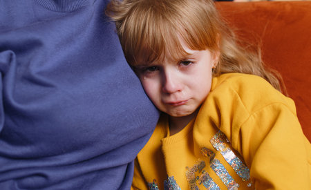 Offended sad girl kid is crying and lying on mother at home. Violence against children in family. Quarrel, bullying at school. Child toddler abuse. Mom hugs, embrace, takes pity on her daughterの写真素材