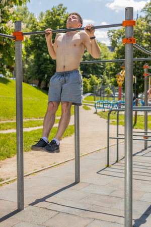 Athletic caucasian topless muscular man doing pull ups exercises on horizontal bar. Young guy...