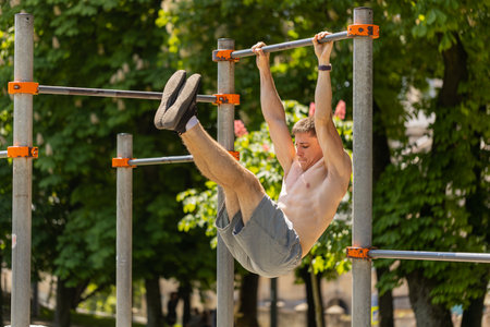 Athletic topless muscular man training abs, doing abdominal crunches, pull-ups exercises on...