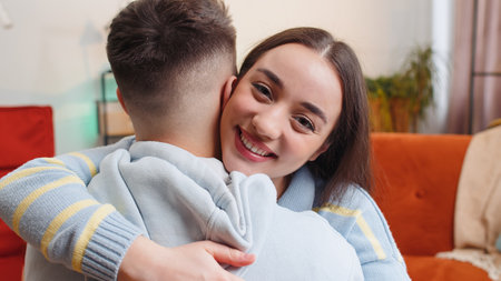 Portrait of woman embracing, hugging man, looking at camera over his shoulder at home. Young...