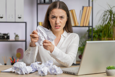 Angry furious business woman working at office throwing crumpled paper having nervous breakdown at work migaine headache stress management, mental distress problems, losing temper, reaction on failureの写真素材