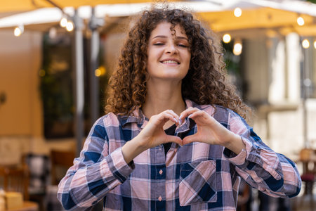 I love you. Young woman makes symbol of love, showing heart sign to camera, express romantic feelings, express sincere positive feelings. Charity, gratitude, donation. Outdoors in urban city streetの写真素材