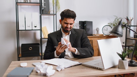 Angry furious indian man working at office throwing crumpled paper, having nervous breakdown at work, migaine, headache, stress management, mental distress problems, losing temper, reaction on failureの写真素材