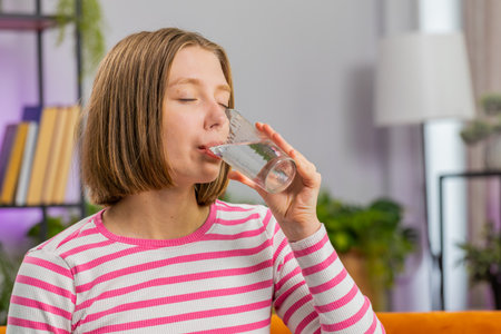 Thirsty brunette woman holding glass of natural aqua make sips drinking still water preventing...