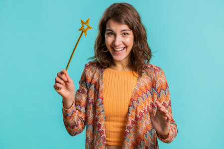 Magician witch young woman gesturing with magic wand fairy stick, making wish come true, casting magician spell, advertising holidays sale discount. Pretty girl isolated on blue studio backgroundの写真素材