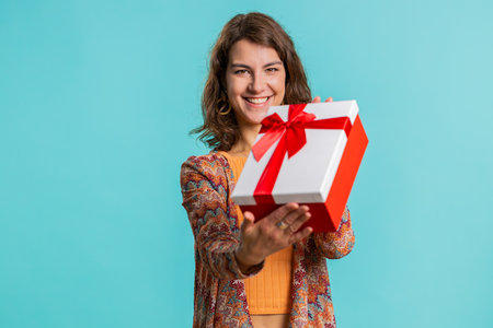 Positive smiling young woman presenting birthday green gift box stretches out hands, offer wrapped...