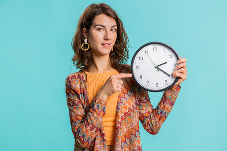 It is your time. Young attractive woman showing time on wall office clock, ok, thumb up, nice good,...