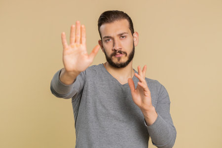 Lebanese man say No hold palm folded crossed hands in stop gesture, warning of finish, prohibited access, declining communication body language, danger. Young guy on beige background. People lifestyleの写真素材