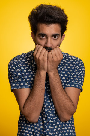 Stressed depressed indian man terrified about danger problems, suffering phobia, anxiety disorder, expresses fear, waving no, insecure, stress, panic. Hindu guy isolated on yellow studio backgroundの写真素材