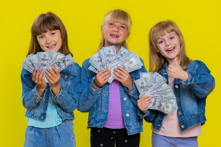 Rich happy teenage girls waving money dollar cash banknotes bills like a fan, success business career, lottery game winner, big income, wealth, donation. Little children sisters. Three siblings kidsの写真素材