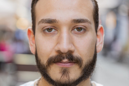 Close-up portrait of happy young man face smiling friendly open eyes glad expression looking at camera dreaming resting relaxation feel satisfied good news outdoors. Bearded guy in sunny city streetの写真素材