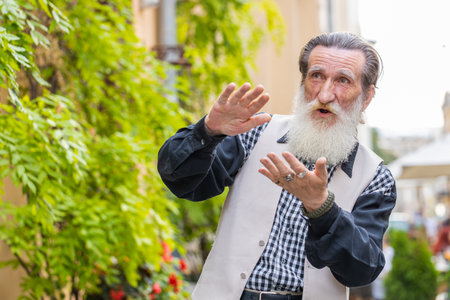 Cheerful rich bearded elderly man showing wasting throwing money around hand gesture, more tips earnings, big profit, win lottery, share, celebrate outdoors. Senior grandfather standing in city streetの写真素材
