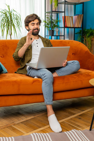 Middle eastern man sitting on couch looking at camera, making video webcam conference call with friends or family enjoying pleasant conversation. Guy laughing waving hello at home room. Verticalの写真素材