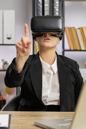 Business woman using virtual reality futuristic technology VR app headset helmet to simulation 3D 360 video at modern office workplace. Excited manager freelancer girl. Remote distant online workingの写真素材