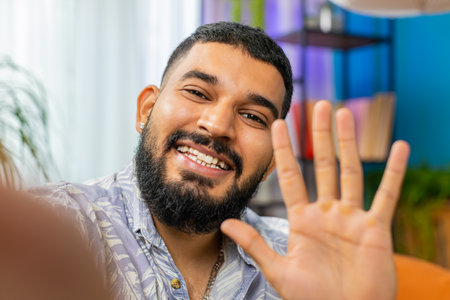 POV view of Indian young man blogger taking selfie on smartphone communicating video call online with subscribers recording stories for social media. Bearded Arabian guy holding mobile phone with handの写真素材