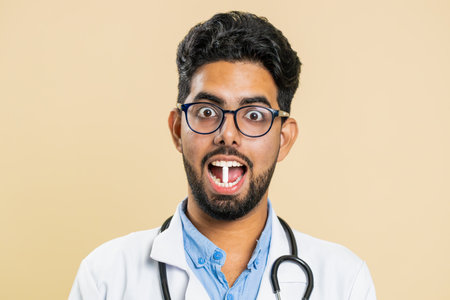 Smiling Indian Hindu doctor man puts of tablet pill white capsule into mouth, recommends drugs immunization cure treatment. Health care. Vitamins for joints, hair, skin, nails. Apothecary pharmacistの写真素材