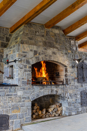 Burning stone barbecue firewood with fire, open brick oven for cooking food meat fish, other dishes indoors in backyard. Restaurant kitchen, pizza oven, bar-b-q grill. Interior construction. Verticalの写真素材