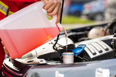 Service worker man pours into car hood engine room windscreen red cleaning washer liquid automobile glass cleaner from canister bottle. Windshield fluid water into windshield washer tank reservoirの写真素材