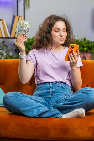 Planning family budget. Smiling woman counting money cash, use smartphone calculate domestic bills at home room. Joyful girl satisfied of income and saves money for planned vacation, gifts. Verticalの写真素材