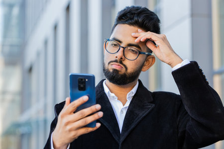Indian businessman use smartphone typing browsing, loses surprised by bad news, fortune loss, fail bankruptcy outdoors. Arabian Hindu freelancer guy in downtown city street. Business people lifestyleの写真素材