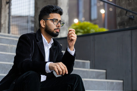 Unhappy sad Indian business man frustrated stress pensive feeling bad after company unemployment lost job problem solution crisis outdoor. Arabian Hindu freelancer guy sitting on stairs downtown cityの写真素材