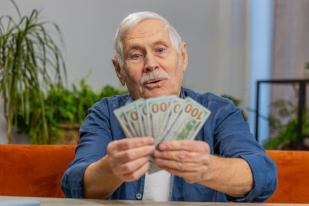 Planning family budget. Happy senior man counting money cash calculate domestic bills at home. Elderly old grandfather satisfied of income salary pension and saves money for planned vacation giftsの写真素材