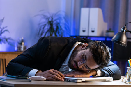 Bored sleepy Indian businessman worker working on laptop computer leaning on hand falling asleep at office table desk. Exhausted tired freelancer workaholic young man. Employment, occupation, worklessの写真素材