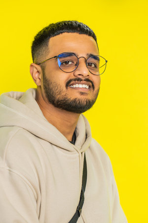 Cheerful lovely happy young Indian man smiling friendly glad expression looking at camera dreaming resting relaxation feel satisfied good news. Arabian bearded guy isolated on yellow studio backgroundの写真素材
