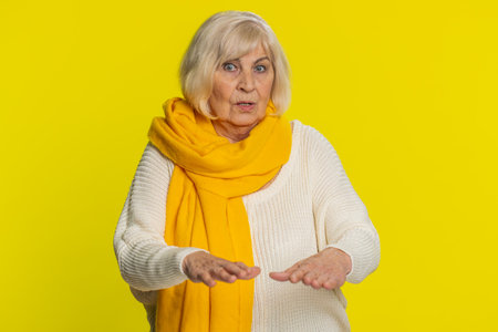 Hey you, be careful. Strict senior woman warning with admonishing hands gesture, saying no be careful scolding, giving advice to avoid danger disapproval sign. Grandmother on yellow studio backgroundの写真素材