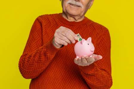 Senior rich old man putting dollar pocket money cash into piggy bank saving for future needs....