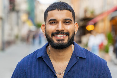 Portrait of happy bearded indian man smiling friendly, glad expression looking at camera dreaming, resting, relaxation feel satisfied good news outdoors. Guy in urban city sunshine street backgroundの写真素材