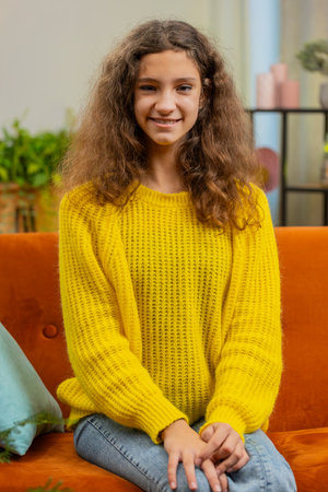 Close-up portrait of happy smiling cheerful Caucasian school girl 15 years old. Young adult lovely child kid student looking at camera at home living room apartment sitting on orange couch. Verticalの写真素材