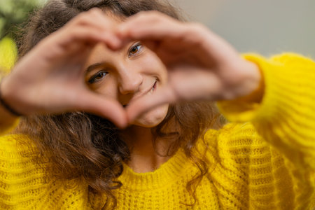 I love you. Portrait of child kid girl makes symbol of love, showing heart sign to camera express romantic feelings express sincere positive feelings. Charity, gratitude, donation. Female teen at homeの写真素材