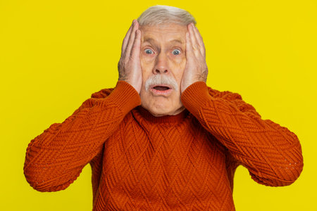 Oh my God, Wow. Excited amazed shocked senior man raising hands in surprise looking at camera with big eyes, shocked by sudden victory celebrating success achievement good news. Grandfather on yellowの写真素材