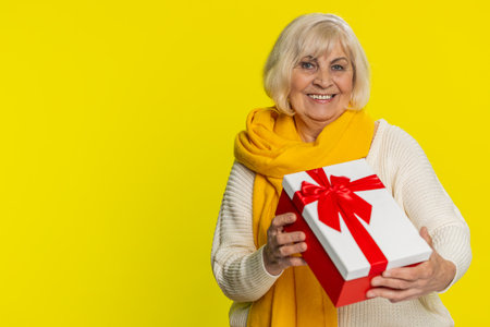 Positive smiling senior woman presenting birthday gift box stretches out hands, offer wrapped present career bonus, celebrating party, promotion discount sale. Elderly mature grandmother. Copy-spaceの写真素材