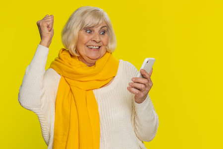 Happy excited senior woman grandmother use smartphone typing browsing shouting say wow yes found out...