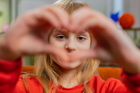 I love you. Caucasian child kid girl makes symbol of love, showing heart sign to camera, express romantic feelings, express sincere positive feelings. Charity, gratitude, donation. Female teen at homeの写真素材