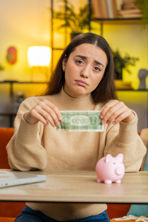Poor young woman insufficient amount of money, holding piggybank and one dollar banknote. Financial...
