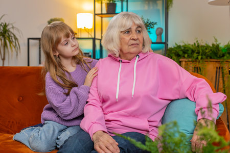 Loving worried kind girl granddaughter consoling sad crying grandmother helping with problem comforting talking to upset senior woman in tears, empathy support embracing sitting on sofa in living roomの写真素材
