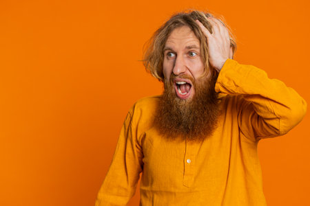 Irritated angry Caucasian man screams from stress tension problems feels horror hopelessness fear surprise shock expresses rage nervous quarrel. Redhead guy isolated on orange background. Copy-spaceの写真素材