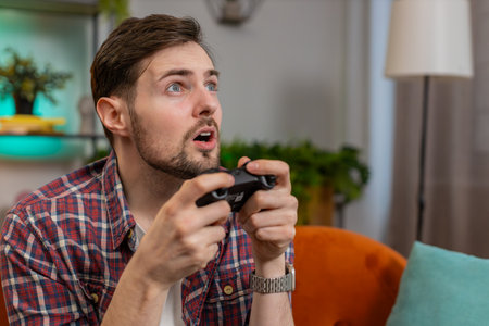Close-up young man using joystick controller playing video console television game fun enjoying sits on couch in living room. Caucasian guy enjoying success winning online game during weekend at homeの写真素材