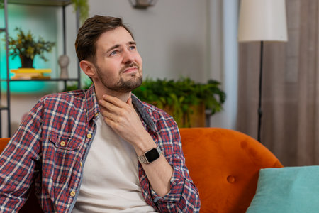 Upset Caucasian ill sick man holds hands over sore throat. Painful neck and frowning, thyroid...