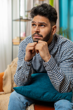 Portrait of sad Indian man guy sits at home looks pensive thinks over life concerns or unrequited love suffers from unfair situation. Problem break up depressed feeling bad annoyed burnout. Verticalの写真素材
