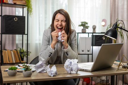 Angry furious business woman working at home office throwing crumpled paper having nervous breakdown...