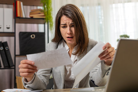Caucasian businesswoman girl opening envelope reading bad news in letter feels upset sitting at home office table. Financial problems, bank debt bill for pay, tax invoice or bankruptcy notification.の写真素材