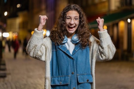Happy child girl clenching fists dancing looking excited at camera celebrate win victory showing...