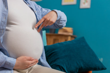 Close-up shot of unrecognizable young pregnant woman walks her fingers over her large belly sitting...