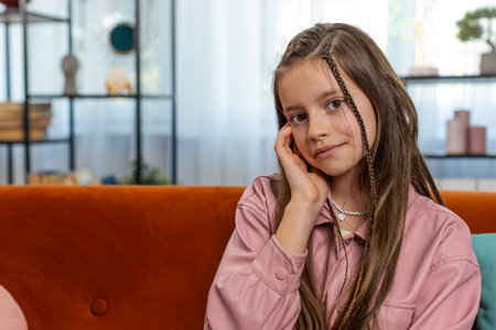 Portrait of happy smiling young girl child sitting on comfy sofa couch looking at camera in living...