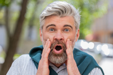 Oh my god, wow. Caucasian mature man looking surprised at camera with big open eyes, shocked by sudden victory, game winning, lottery goal achievement, good news outdoors. Guy on city sunshine street.の写真素材