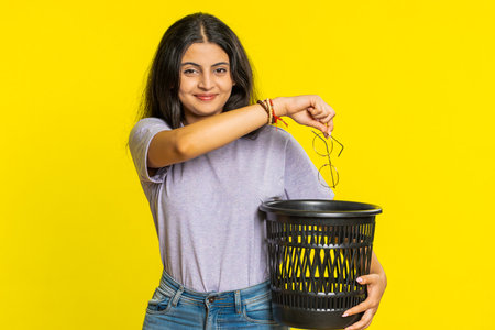 Indian young woman taking off throwing out glasses into bin after medical vision laser treatment...